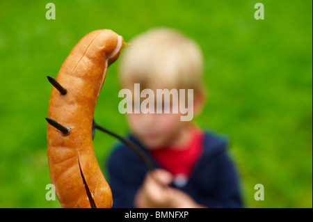 Kind blonde junge Braten / grillen Würstchen über dem offenen Feuer im freien Stockfoto