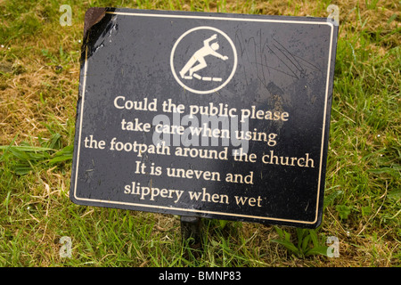 Ein Schild warnt die Öffentlichkeit über die Gefahren des Gleitens auf dem unebenen Weg in einer englischen Kirchhof. Stockfoto