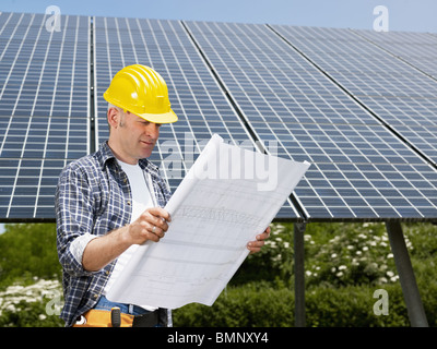 Elektriker mit Blaupausen in Solarkraftwerk Stockfoto