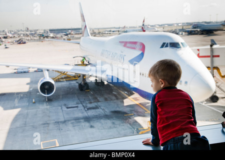 Ein kleiner Junge trägt einen roten und blauen Hemd schauen aus dem Fenster auf den Laufsteg am terminal 5 Heathrow Flughafen Stockfoto