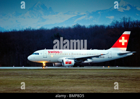 Ein Swiss Airbus A319-112 Rollen für nehmen Sie an einem Winterabend am Genfer Flughafen, den Alpen im Hintergrund Stockfoto