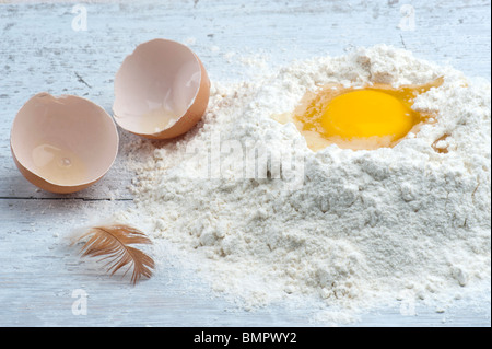 Eine gebrochene Ei In etwas Mehl mit der Schale und eine Henne Feder zur Seite Stockfoto