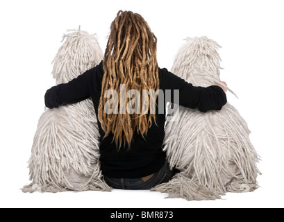 Ansicht von hinten von zwei weißen schnurgebundenen standard Pudel und Frau mit Dreadlocks sitzen vor weißem Hintergrund Stockfoto