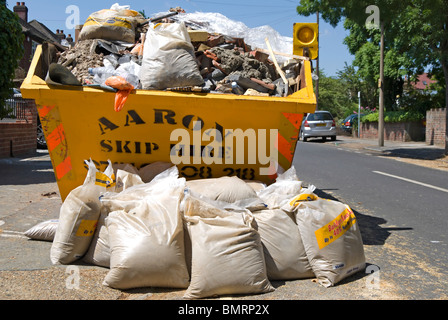 des Erbauers überspringen gefüllt mit Müll und Säcke mit Sand im Vordergrund Stockfoto