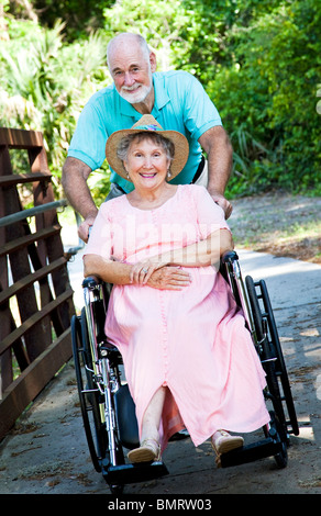 Ältere Mann seine behinderte Frau durch den Park in einen Rollstuhl zu schieben. Stockfoto