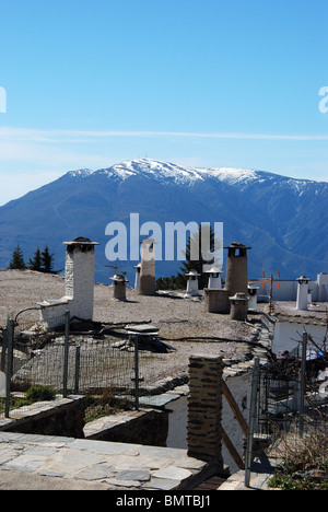 Blick über die Dächer in Richtung Schnee bedeckt Berge der Sierra Nevada, Capileira, Las Alpujarras, Provinz Granada, Spanien. Stockfoto