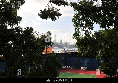 Blick durch Bäume, einen Tennisplatz, in Richtung Victoria Harbour und Kowloon Wolkenkratzern, Victoria Park, Causeway Bay, Hong Kong Stockfoto