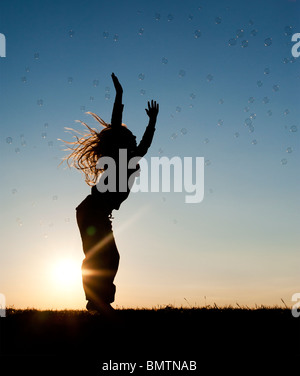 Young Girl energetisch Spaß springen und fangen Luftblasen bei Sonnenuntergang. Silhouette Stockfoto