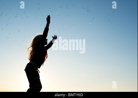 Young Girl energetisch Spaß springen und fangen Luftblasen bei Sonnenuntergang. Silhouette Stockfoto