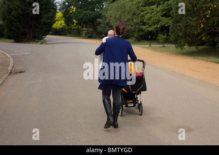 Eine einsame Mutter auf eine unbekannte Reise trägt ihr Säugling Baby in einem Londoner Park. Stockfoto