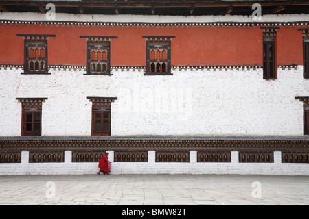 Ein Mönch, zu Fuß entlang einer langen Reihe von Gebetsmühlen auf eine Mauer des Klosters Tashichho Dzong in Thimpu, Bhutan. Stockfoto