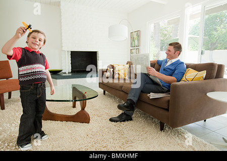 Kleiner Junge spielt mit Spielzeug Flugzeug, Vater lesen Zeitung Stockfoto