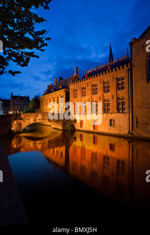 Historische Altbauten und eine Fußgängerbrücke, beleuchtet in der Dämmerung, spiegeln sich in einem Kanal. Stockfoto
