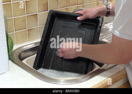 Kaukasischen Mann Abwasch ein schwarzer Emaille Grillpfanne in einer Küchenspüle Modell veröffentlicht Stockfoto