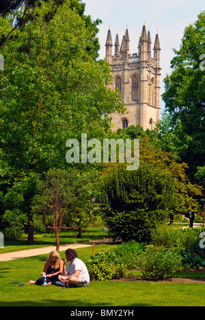 Ein paar genießen Sie die Sommersonne im Botanischen Garten, Oxford, mit dem Turm des Magdalen College im Hintergrund Stockfoto