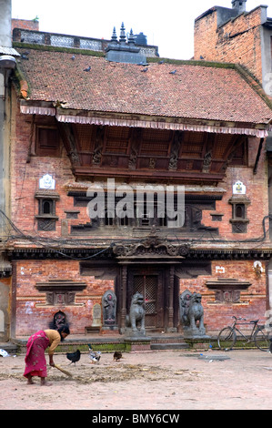 Eine Frau fegt den Hof vor einem spektakulären alten Gebäude, Yatkha Bahal, Kathmandu, Nepal. Stockfoto