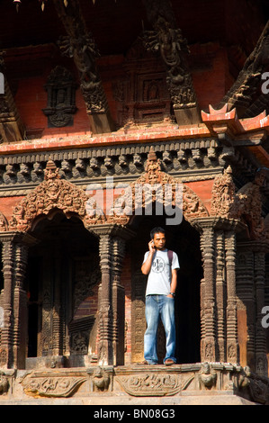 Ein junger Mann spricht auf einem Mobiltelefon am Eingang zum Vishwanath Tempel, Durbar Square, Patan, Nepal. Stockfoto