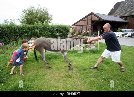 Ein Mann mit Kindern versuchen, einen störrischen Esel verschieben Stockfoto