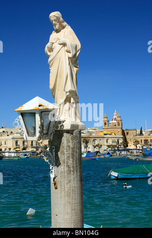 Eine Statue des Schutzheiligen der Fischer St Andrew steht stolz im Hafen von Marsaxlokk, Marsaxlokk, Malta Stockfoto