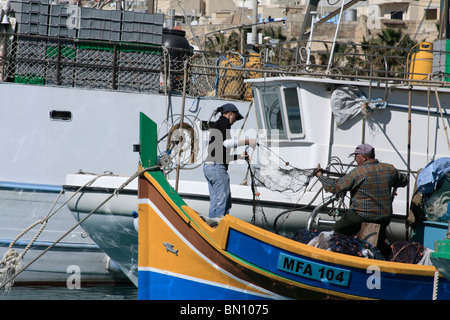 Vater und Tochter vorbereiten ihrer Fischernetze auf einem bunten traditionellen maltesischen Fischerboot. Marsaxlokk, Malta Stockfoto