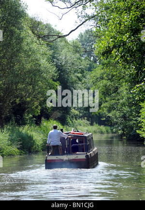 EIN MANN STEUERT EIN NARROWBOAT AN EINEM BRITISCHEN KANAL, UK Stockfoto