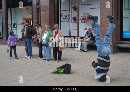 Eine kleine Menschenmenge beobachten einen Mann steht auf dem Kopf stehend mit dem Kopf in einen Eimer auf Princes Street, Edinburgh. Stockfoto