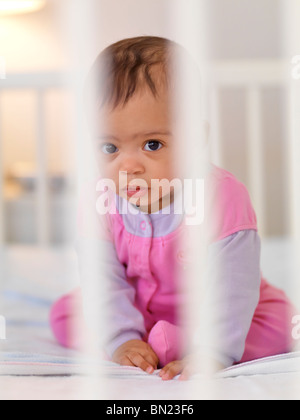 Niedliche sieben Monate alten Baby Mädchen sitzen in einer Krippe hinter Gittern Stockfoto