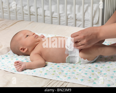 Sechs Wochen alten niedlichen Baby-jungen auf einem Bett liegend, während Mutter seine Windel ändert Stockfoto