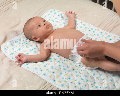 Sechs Wochen alten niedlichen Baby-jungen auf einem Bett liegend, während Mutter seine Windel ändert Stockfoto