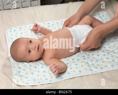 Sechs Wochen alten niedlichen Baby-jungen auf einem Bett liegend, während Mutter seine Windel ändert Stockfoto