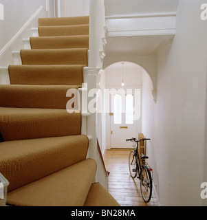 Cremefarbene Teppich auf Treppe im Weißen Saal mit Holzboden und Fahrrad an die Wand gelehnt Stockfoto