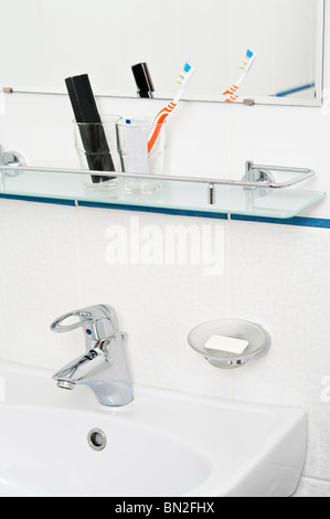 Bad-Accessoires: Zahnpasta und Bürste auf Glasregal. Wasserhahn in Schüssel Stockfoto