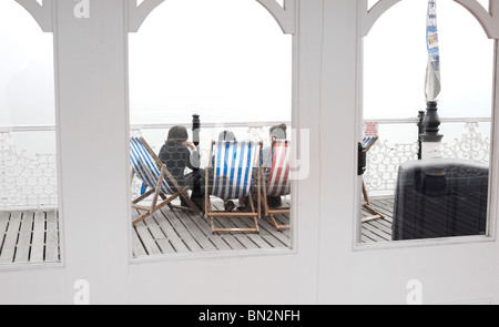 Durch die Glasfenster von Brighton Pier Touristen gesehen sitzen auf den Liegestühlen Stockfoto