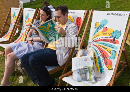 Mann liest Zeitung und Frau entspannt sitzen in Liegestühlen in der Sonne bei Hay Festival 2010 Hay on Wye Powys Wales UK Stockfoto