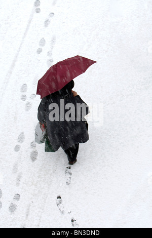 Frau mit Sonnenschirm und Einkaufstaschen zu Fuß durch den Schnee, Vogelperspektive Stockfoto