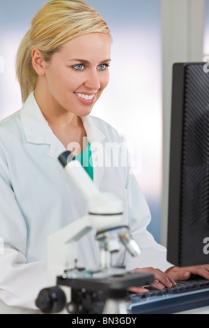 Eine lächelnde medizinische oder wissenschaftliche Forscher oder Frau Ärztin mit einem Computer in einem Labor mit Mikroskop Stockfoto