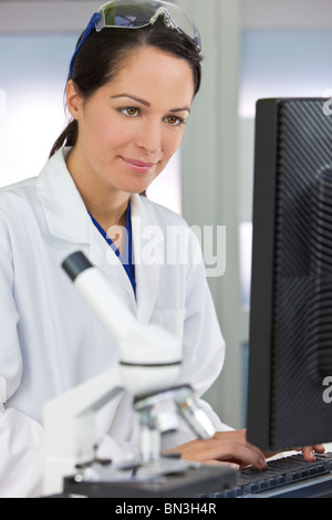 Eine lächelnde medizinische oder wissenschaftliche Forscher oder Frau Ärztin mit einem Computer in einem Labor mit Mikroskop Stockfoto