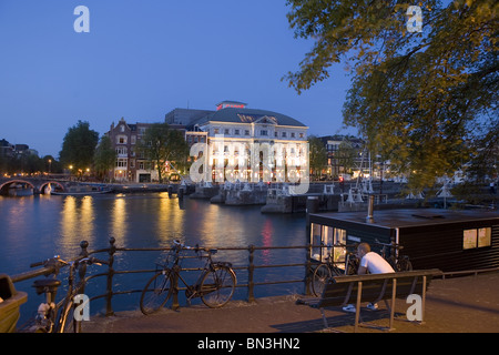Mann sitzt auf einer Bank an einem Fluss, Carre Theater im Hintergrund, Amsterdam, Niederlande Stockfoto