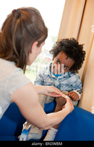 Kindergärtnerin, ein Pflaster auf Jungs Bein anwenden Stockfoto