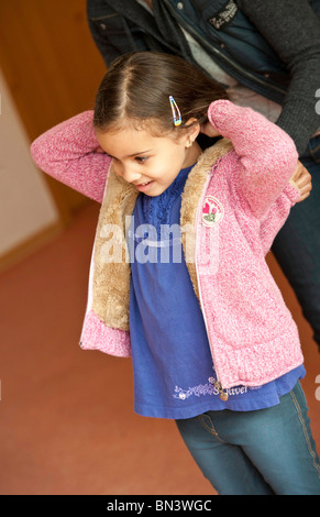Kindergärtnerin, die jungen Mädchen ihre Jacke anziehen helfen Stockfoto