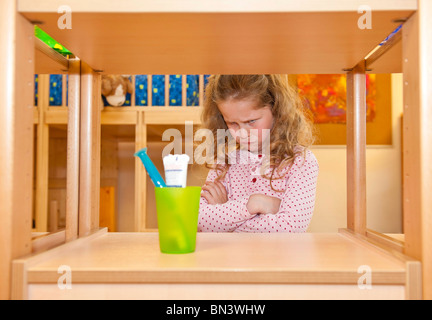 Kleines Mädchen Arme kreuzen und Zahnbürstenhalter auf ein Regal Stockfoto