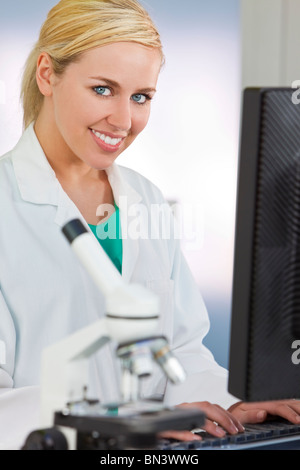 Eine lächelnde medizinische oder wissenschaftliche Forscher oder Frau Ärztin mit einem Computer in einem Labor mit Mikroskop Stockfoto