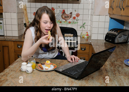 Teenager-Mädchen Frühstück Toast essen gekochtes Ei und Orangensaft während der Arbeit an ihrem Laptop-computer Stockfoto