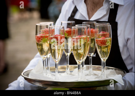 Nicht identifizierbarer Kellner, der ein rundes silbernes Tablett mit Gläsern mit Champagner und Erdbeeren hält Stockfoto