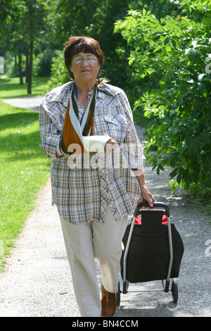 Ältere Dame im Park spazieren, mit gebrochenen Arm in der Schlinge Stockfoto