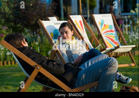 Junges Paar sitzen in Liegestühlen entspannen und reden in der Sommersonne am Hay Festival 2010 Heu auf Wye Powys Wales UK Stockfoto