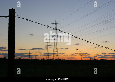 Stacheldraht und elektrische Leitungen sind in den Sonnenuntergang über einem Feld Landwirtschaft gesehen. Stockfoto