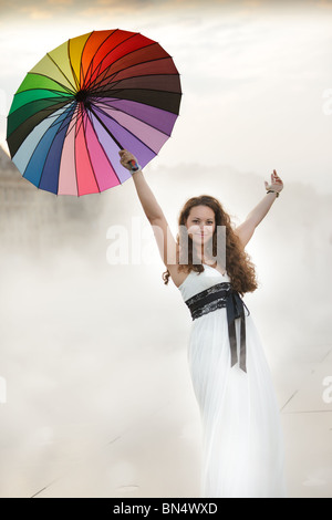 Frau hält Regenbogen Regenschirm und Arme in dichtem Nebel Stockfoto
