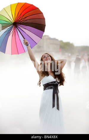 freudige hübsche Frau mit Regenbogen Regenschirm im Nebel Stockfoto