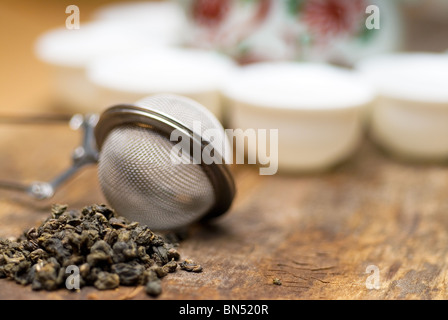 trockenen grünen chinesischen Tee-Set, mit Sieb Closeup, Tassen und Teekanne auf Hintergrund über alte Holzplatte Stockfoto